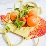A collection of oranges and green leaves in a colorful net bag on a bright surface.