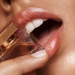 Artistic close-up of lips gently biting a perfume bottle, showcasing elegance.
